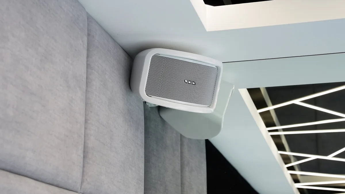 A compact white speaker bracketed neatly under a ceiling edge