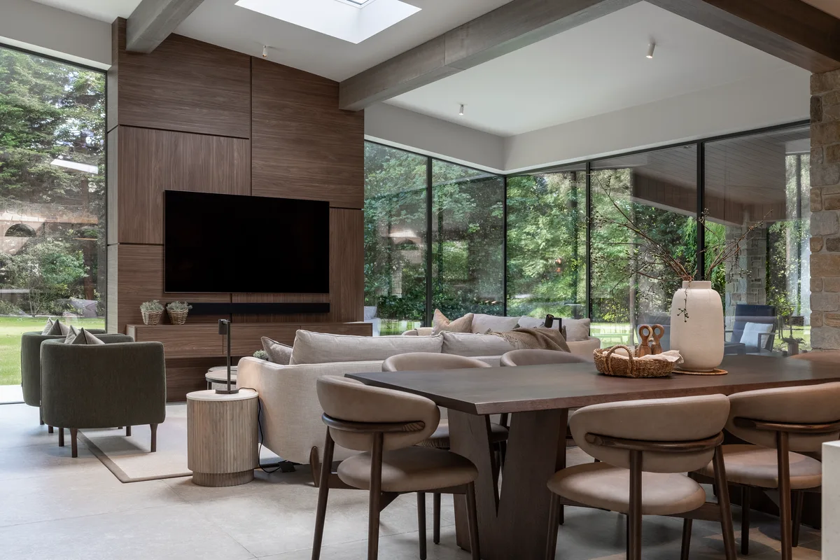 An open-plan living and dining space with concealed ceiling speakers and a screen set into walnut joinery