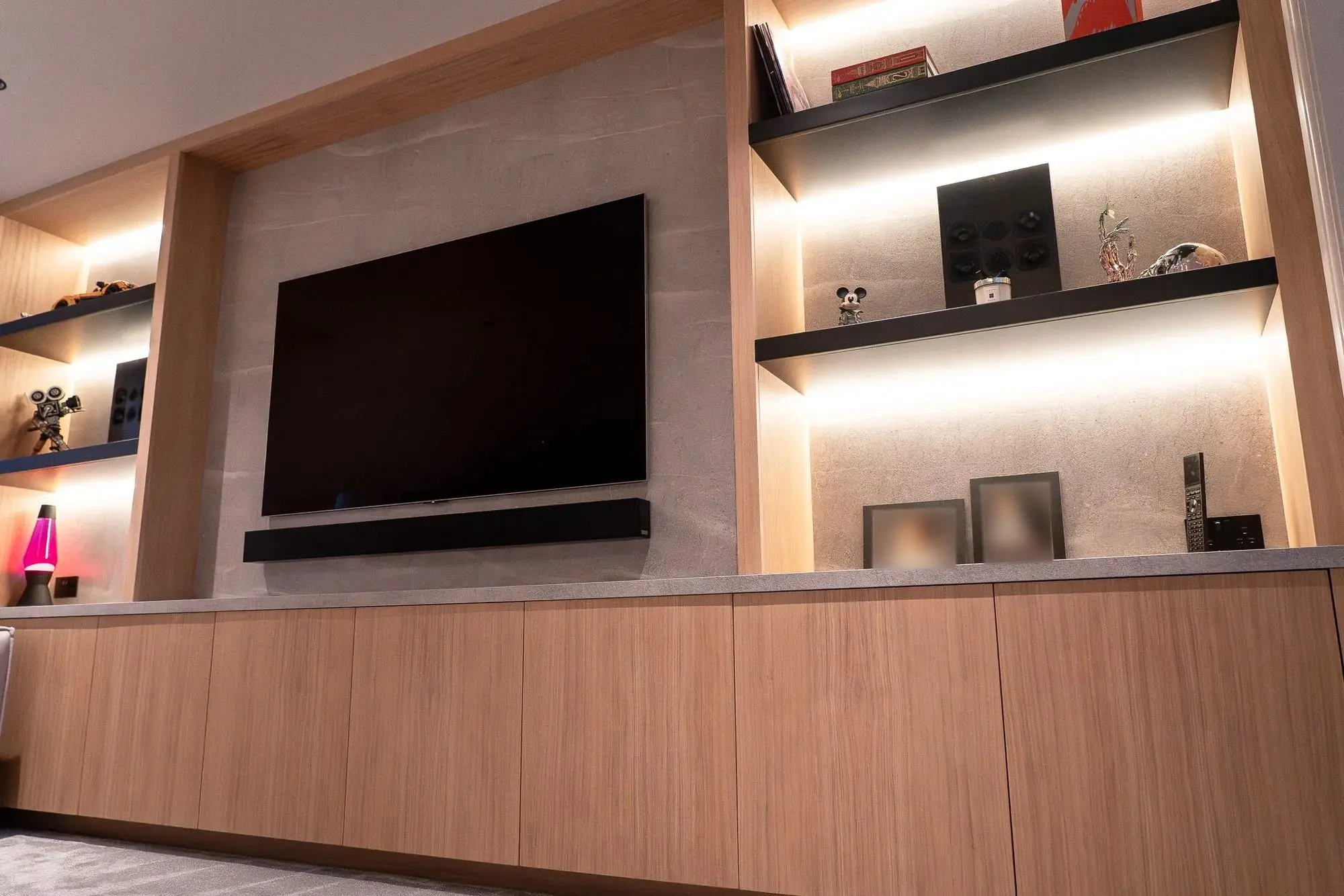 The finished media wall: a screen on a stone-effect panel, framed by oak joinery with lit shelving either side