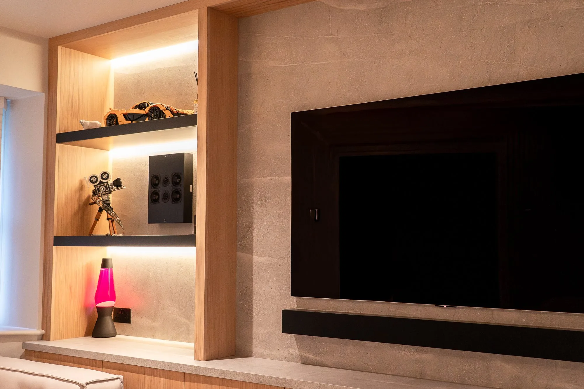 An Artcoustic speaker on a lit shelf beside the screen and soundbar