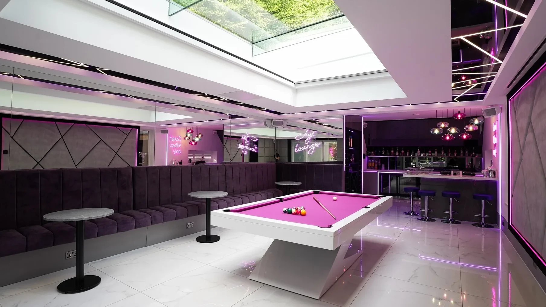 A games room with the roof light blind open, daylight and planting visible through the glass
