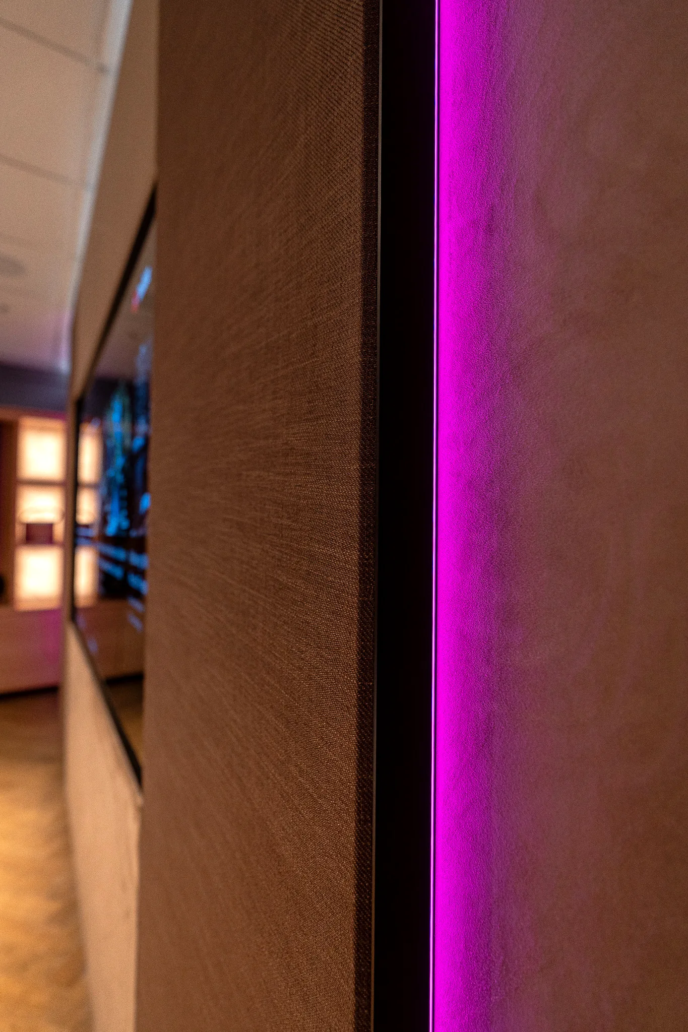 The edge of an acoustic fabric panel lit from behind, the room beyond falling away out of focus.