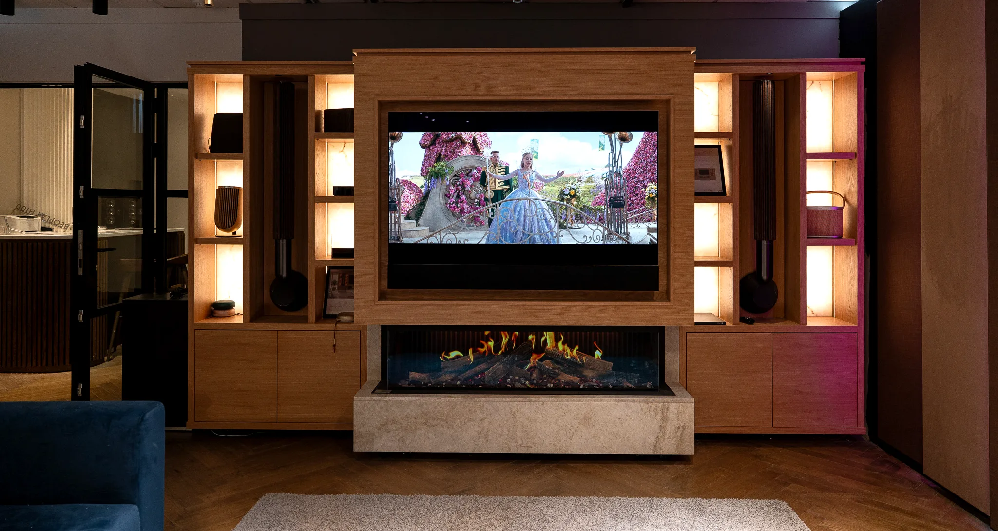 An oak media wall seen straight on, with a television framed in timber above a linear fireplace and backlit onyx shelving to either side.