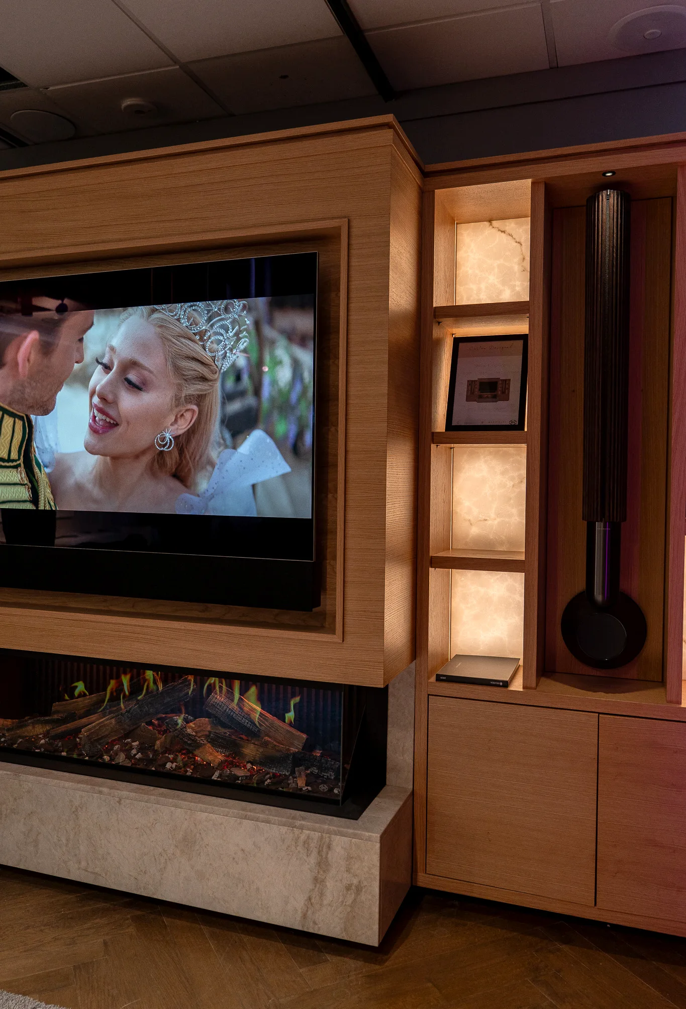 Close view of the timber frame around a television, the fireplace below it, and the backlit onyx shelving in the cabinetry alongside.