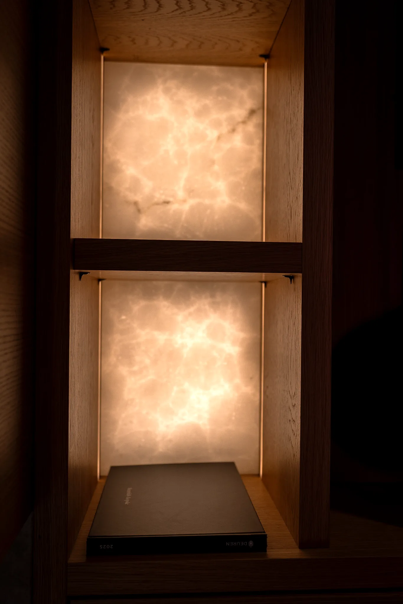 Two backlit onyx display niches in oak cabinetry, the lower one holding a slimline media player.